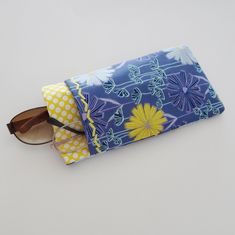 "This double pocket sleeve or case is a great organizer for 2 pairs of glasses. This case is made up in a blue, aqua, purple and yellow floral design cotton print fabric with a contrast yellow polka dot fabric. There is a purple cotton fabric lining. The main pocket will accommodate your sun glasses or eye glasses and the outside pocket is an easy slip in for your readers or a second pair of glasses. The pockets are also a designed to fit your cell phone and one pair of glasses, should you choos Blue Rectangular Case For Everyday Use, Blue Cases With Pen Holders For Daily Use, Blue Cases With Pen Holders, Blue Zipper Pouch Case For Storage, Sunglasses Cases To Sew, Blue Rectangular Case For Personal Use, Fabric Sunglasses Pouch, Sew Sunglasses Case, Blue Zipper Pouch Case