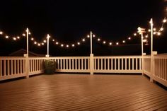 an outdoor deck with string lights on the posts and potted plant in the middle