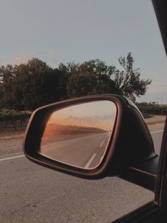 the rear view mirror of a car is reflecting trees in it's side view mirror