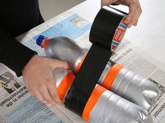 a person is using an orange and black water bottle holder to hold two bottles on top of newspaper pages