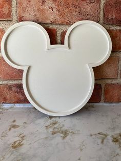 a white mickey mouse shaped plate sitting on top of a counter next to a brick wall