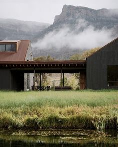 a house sitting on top of a lush green field next to a lake and mountains