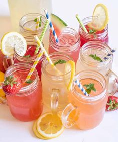 several mason jars filled with different types of drinks and strawberries next to lemons