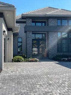 a house that has a brick driveway in front of it and the sun shining through the windows