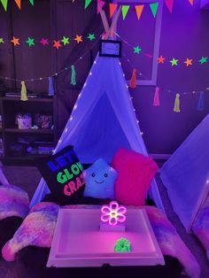 a teepee tent is lit up with purple and green lights in the background, while a pink flower sits on a white tray