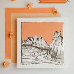 an orange card with a drawing of mountains in the background and pencils next to it