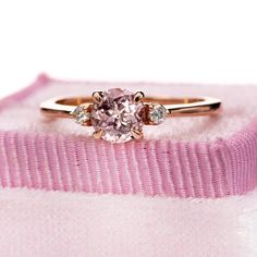 a pink diamond engagement ring sitting on top of a pink velvet cushioned box with two diamonds in it