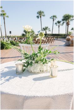 the table is set with flowers and candles for an outdoor wedding reception in front of palm trees