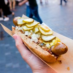 a person holding a hot dog with pickles and onions on it's bun