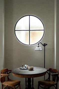 a round window in the wall above a table with two chairs and a lamp on it