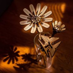 two wooden flowers in a glass vase on a wood table with sunlight shining through the window