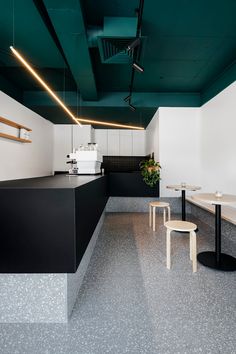 an empty restaurant with black counter tops and white walls, along with two stools