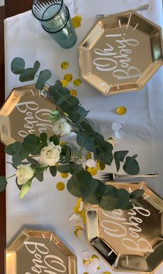 the table is decorated with gold and white plates, silver trays, flowers and greenery