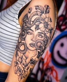 a woman's face with flowers and snakes around her head on the right arm