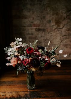 a vase filled with lots of flowers sitting on top of a wooden table next to a brick wall