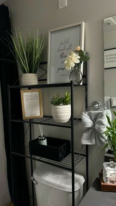 a bathroom with a toilet, plants and pictures on the shelf above it's tank