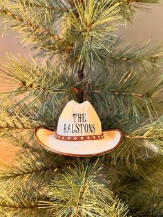 a cowboy hat ornament hanging from a pine tree with the words, the ralastons on it