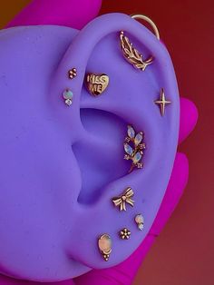 a person's hand holding up a purple ear with various jewelry pieces on it