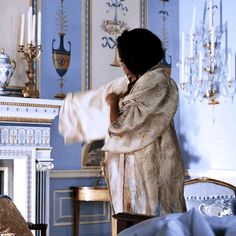 a woman standing in front of a fire place holding a blanket over her shoulder and looking at the fireplace