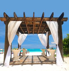 an outdoor gazebo with white drapes on the beach