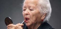 an older woman brushing her teeth in front of a magnifying mirror with one hand