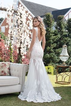 a woman standing in front of a couch wearing a wedding dress with an open back