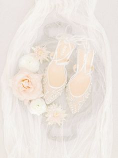 wedding shoes and flowers on a white cloth with tulle veils in the background