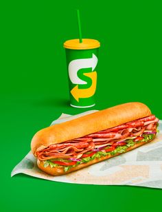 a sub sandwich and a drink on a green background