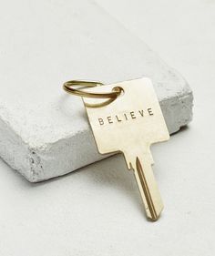 a gold keychain with the word believe on it sitting on top of a stone block