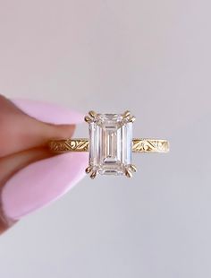 a close up of a person's hand holding a ring with an emerald stone