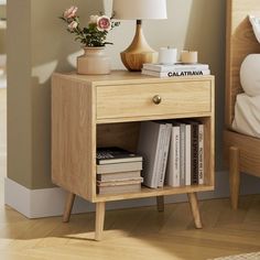 a nightstand with some books on it next to a lamp and a bed in a room