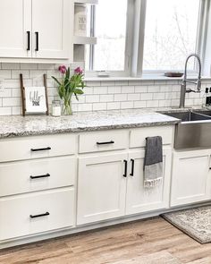 a kitchen with white cabinets and marble counter tops, an island in the middle has flowers on it