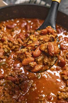 a spoon full of chili and meat in a pot with the lid open to show it's contents