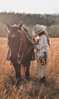 a woman standing next to a brown horse on top of a dry grass covered field