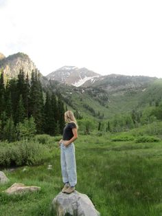 a woman standing on top of a rock in the middle of a grass covered field