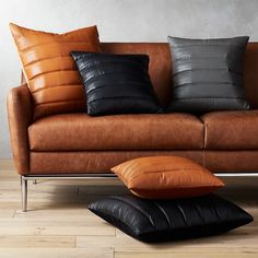 a brown leather couch with two black and one tan pillows on it's back