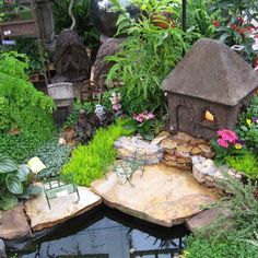 a small pond surrounded by lots of plants and other things in the yard with a little house on top