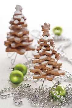 two small christmas trees made out of cookies on a white table with silver beads and green apples