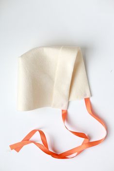 a white hat with an orange ribbon tied around it on a white surface, next to a pair of scissors