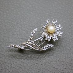 This charming vintage brooch, crafted from 835 silver, features a beautifully stylized daisy flower adorned with marcasite stones and a faux pearl center. A fine example of 1950s mid-century jewelry, this small silver brooch is an exquisite piece of heritage jewelry, perfect for adding a touch of elegance to any outfit. The brooch will be shipped in a gift box. The brooch measures 1 3/5" long by 2/3" wide (4.0 cm  x  1.74 cm) Weight: 4.3 grams The pearl measures over 1/5" (5.7 mm) in diameter Ro Vintage Flower Brooches For Anniversary, Silver Vintage Flower Brooches, Vintage Silver Flower Brooches, Mid-century Flower Jewelry Gift, Vintage Silver Flower Pins, Marcasite Jewelry, Heritage Jewellery, Mid Century Jewelry, Silver Brooch