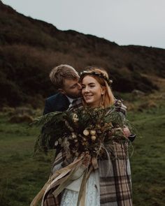 a man and woman standing next to each other in the grass with flowers on their heads