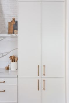 a kitchen with white cupboards and gold handles on the doors, along with wooden utensils