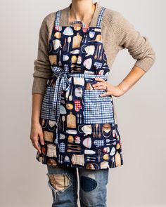 a woman standing with her hands on her hips wearing an apron that has food and utensils all over it