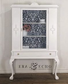 a white cabinet with floral wallpaper on the front and bottom, sitting next to a wooden floor