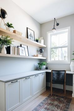 a room with some shelves and plants on the wall next to a chair in front of a window