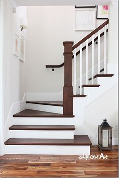 a white staircase with wooden handrails and wood flooring next to a lantern