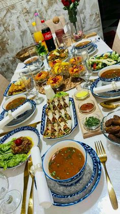 a table full of food and silverware on top of a white cloth covered table