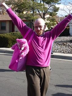 an older man is walking down the street with his arms in the air and pink letters above him