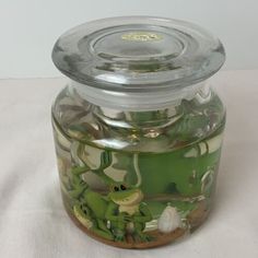 a glass jar filled with lots of green frog images on the lid and bottom, sitting on a white tablecloth