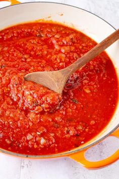 a wooden spoon in a pot filled with marinara sauce on top of a table